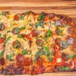 Immagine di una pizza in teglia con impasto poco lievitato e bordo sottile, evidenziando il problema di lievitazione.