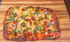 Immagine di una pizza in teglia con impasto poco lievitato e bordo sottile, evidenziando il problema di lievitazione.