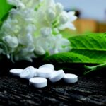 Aspirina disciolta in acqua per piante, con foglie verdi e un vaso sullo sfondo.