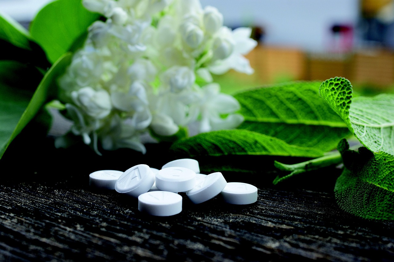 Aspirina disciolta in acqua per piante, con foglie verdi e un vaso sullo sfondo.